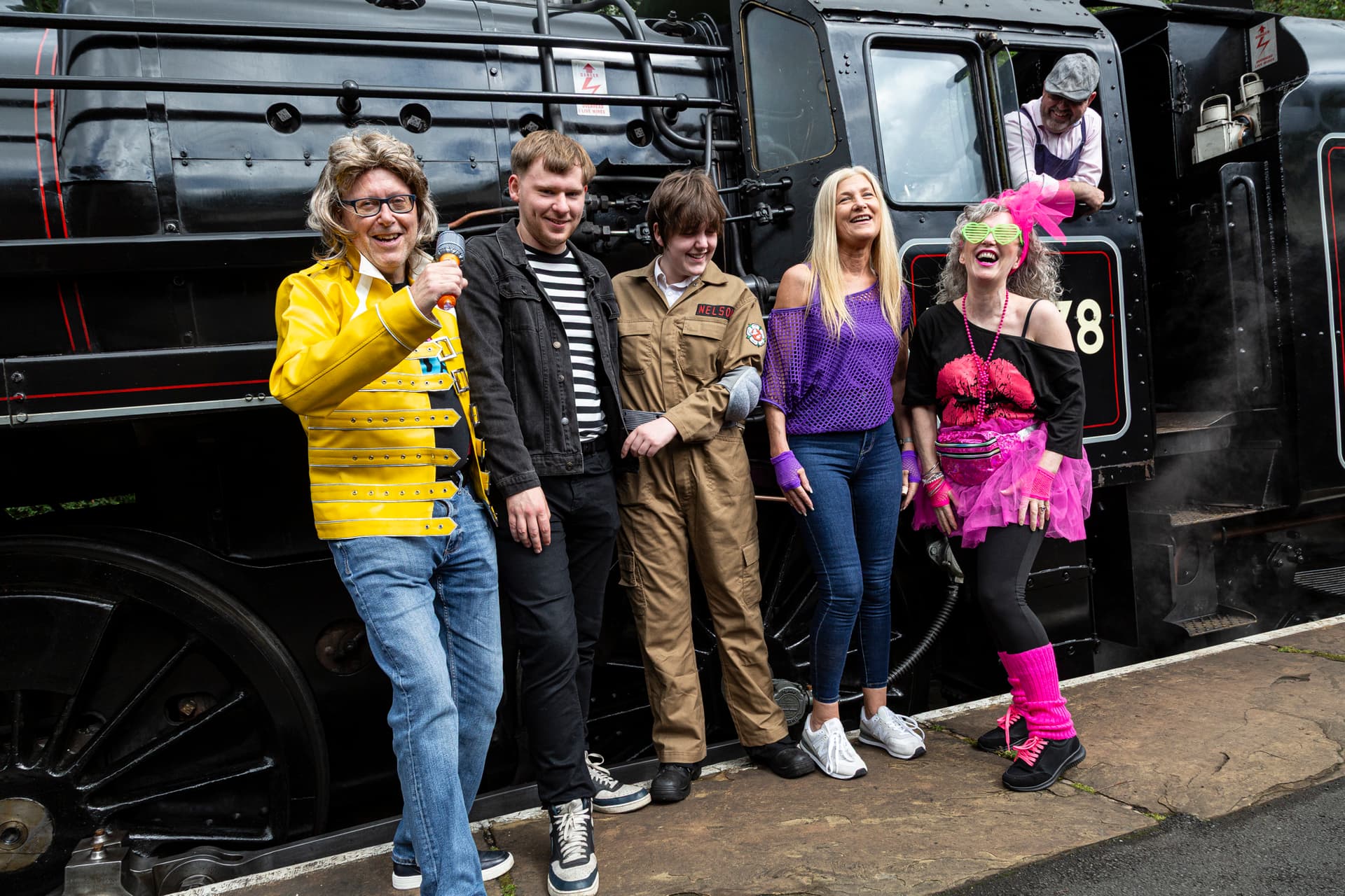 Group in costumes laughing beside vintage steam train