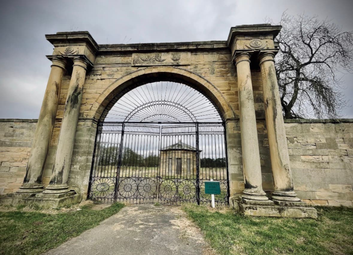Historic stone archway with iron gate and distant pavilion