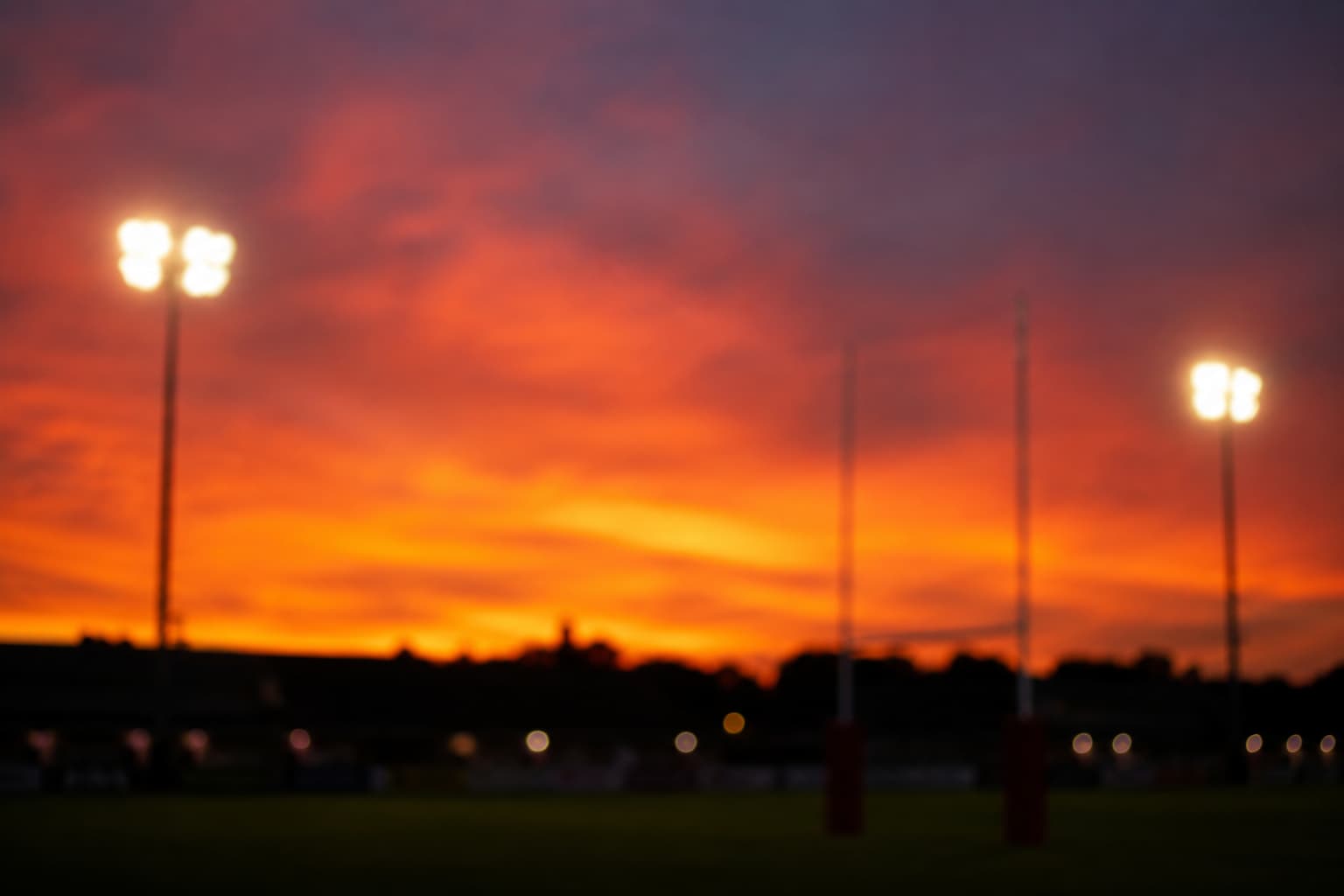 Rugby field at sunset with vibrant orange sky and floodlights