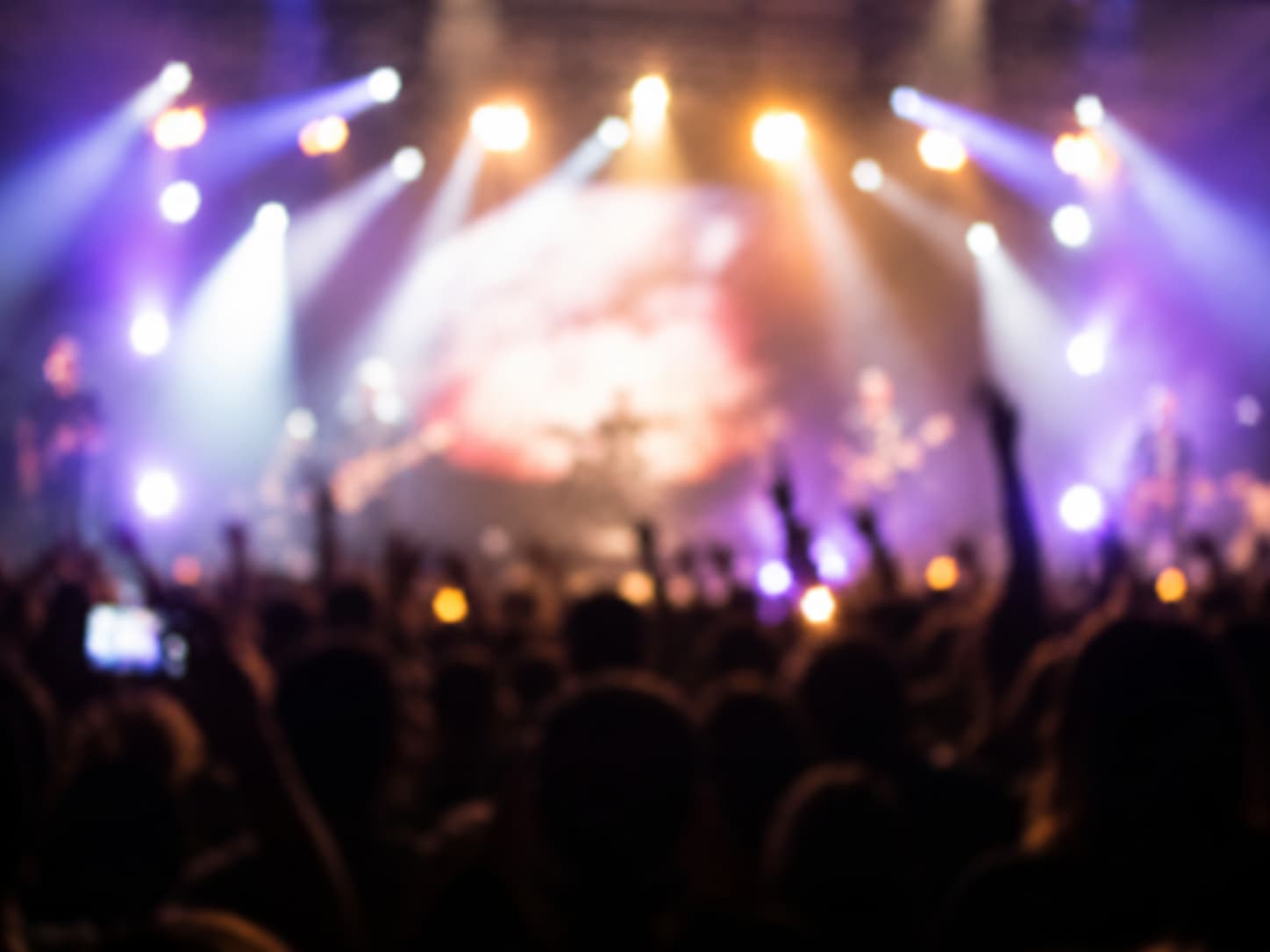 Blurred concert scene with vibrant stage lights and cheering crowd