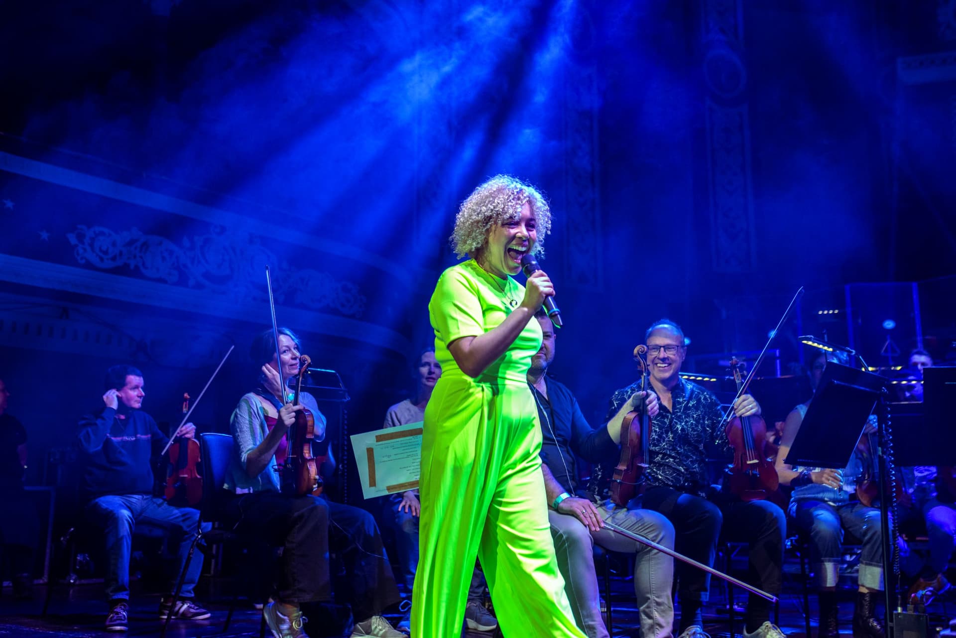 Singer in bright green outfit on stage with orchestra