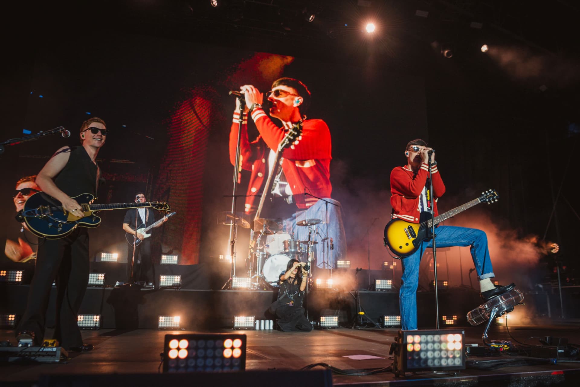 Rock band performing on stage with vibrant lights and large screen
