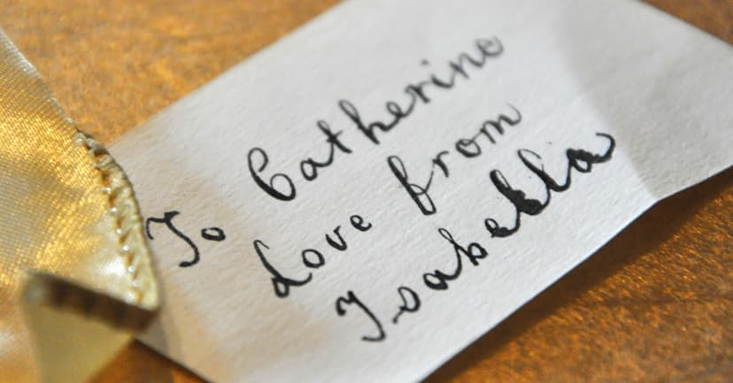 A handwritten note on textured paper, tied with a ribbon, expressing love from Isabella to Catherine.