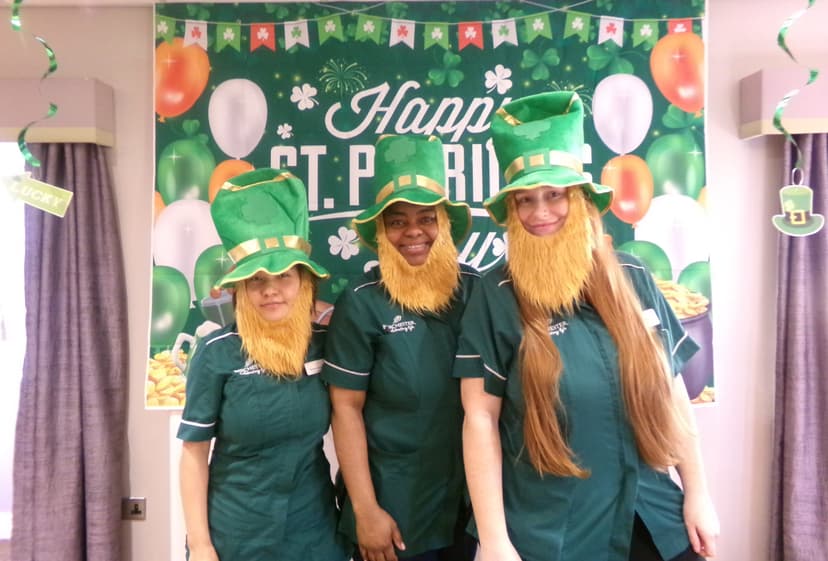 Three people in green outfits and leprechaun hats at a St. Patrick's Day celebration