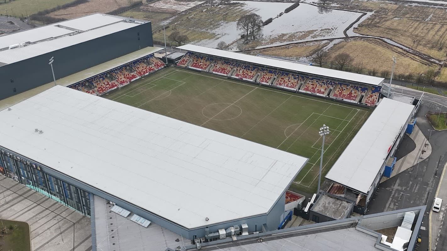 Aerial view of a modern football stadium with red seats and surrounding fields