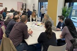 Group of people in a discussion around a white table in a bright room