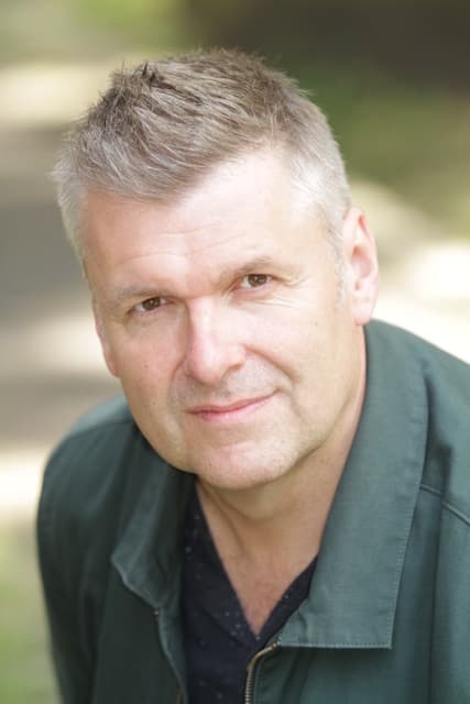 Man with short grey hair wearing a green jacket outdoors