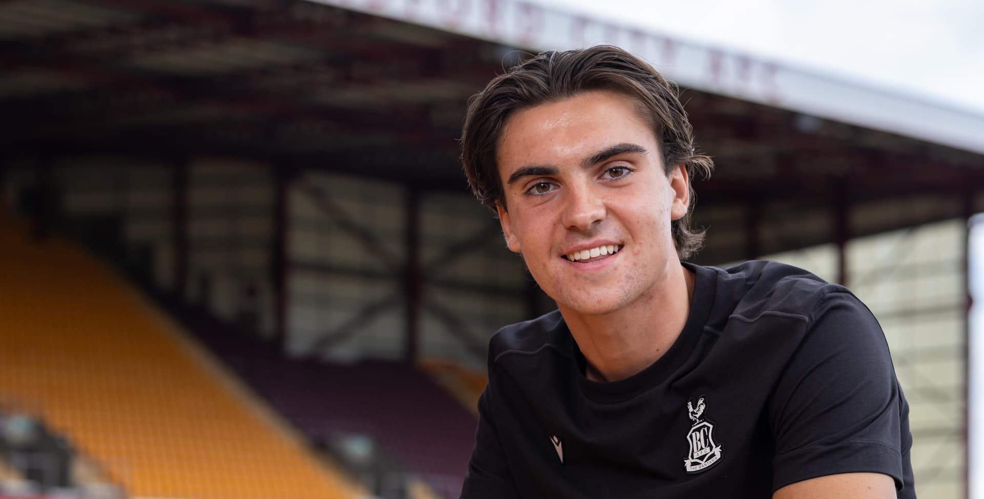 Young man in black shirt smiling at a sports stadium