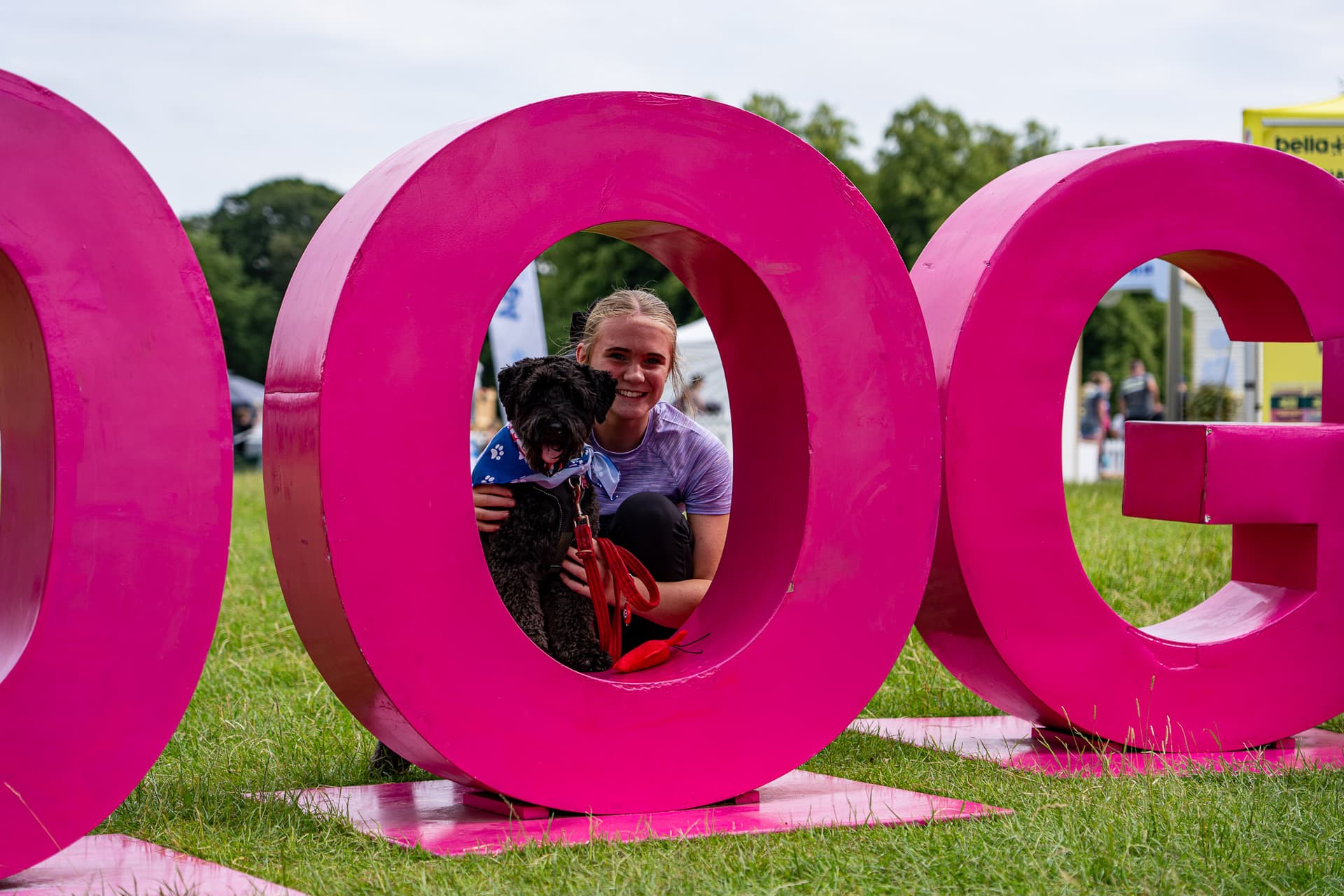 Person and dog sitting inside large pink letters on grass