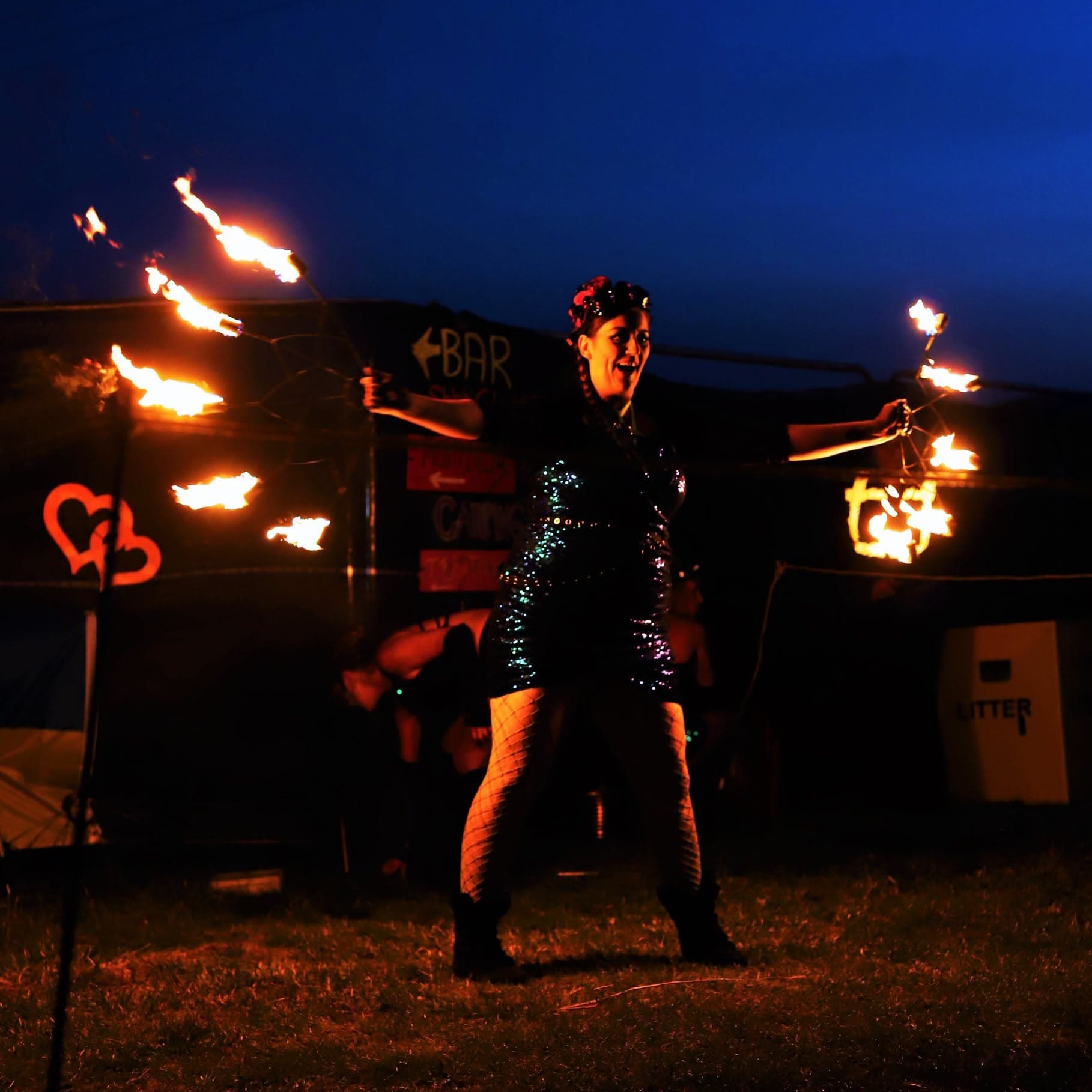 Performer in sequined dress twirling fire sticks at night festival