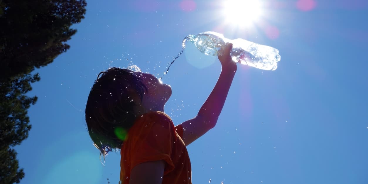 Child drinking from a water bottle under bright sun