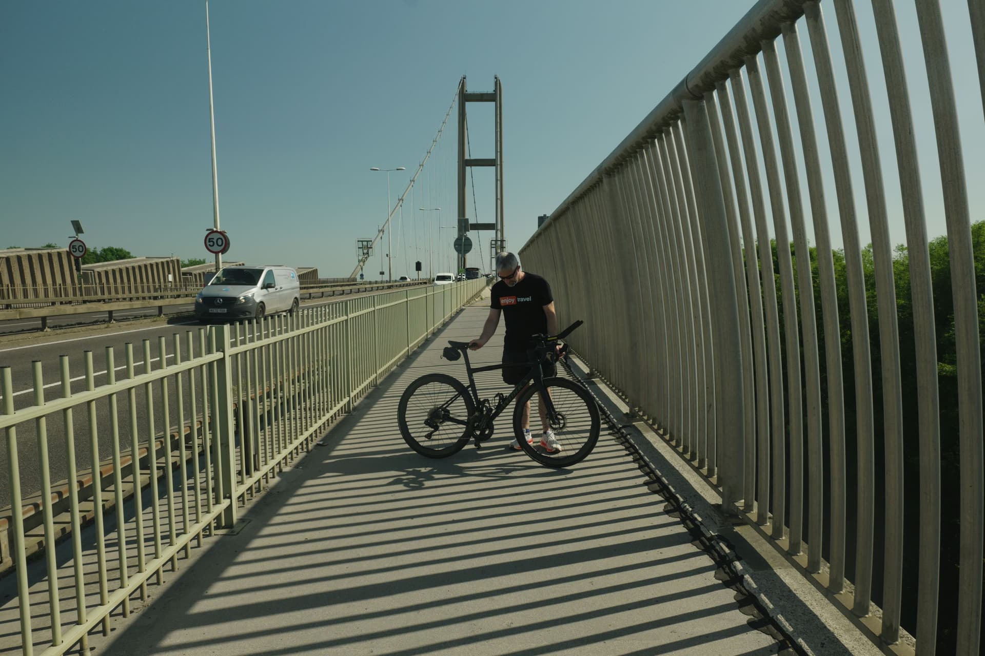 Cyclist resting on Humber Bridge footpath with shadows