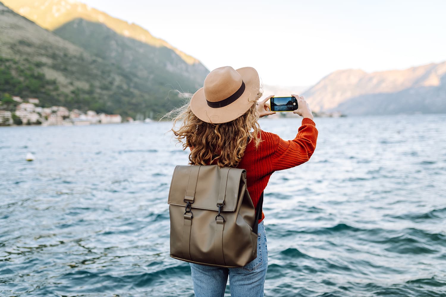 Woman in hat photographing scenic lake with mountains