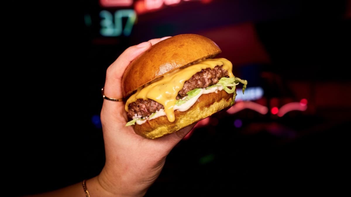 Hand holding a cheeseburger with lettuce and a glossy bun