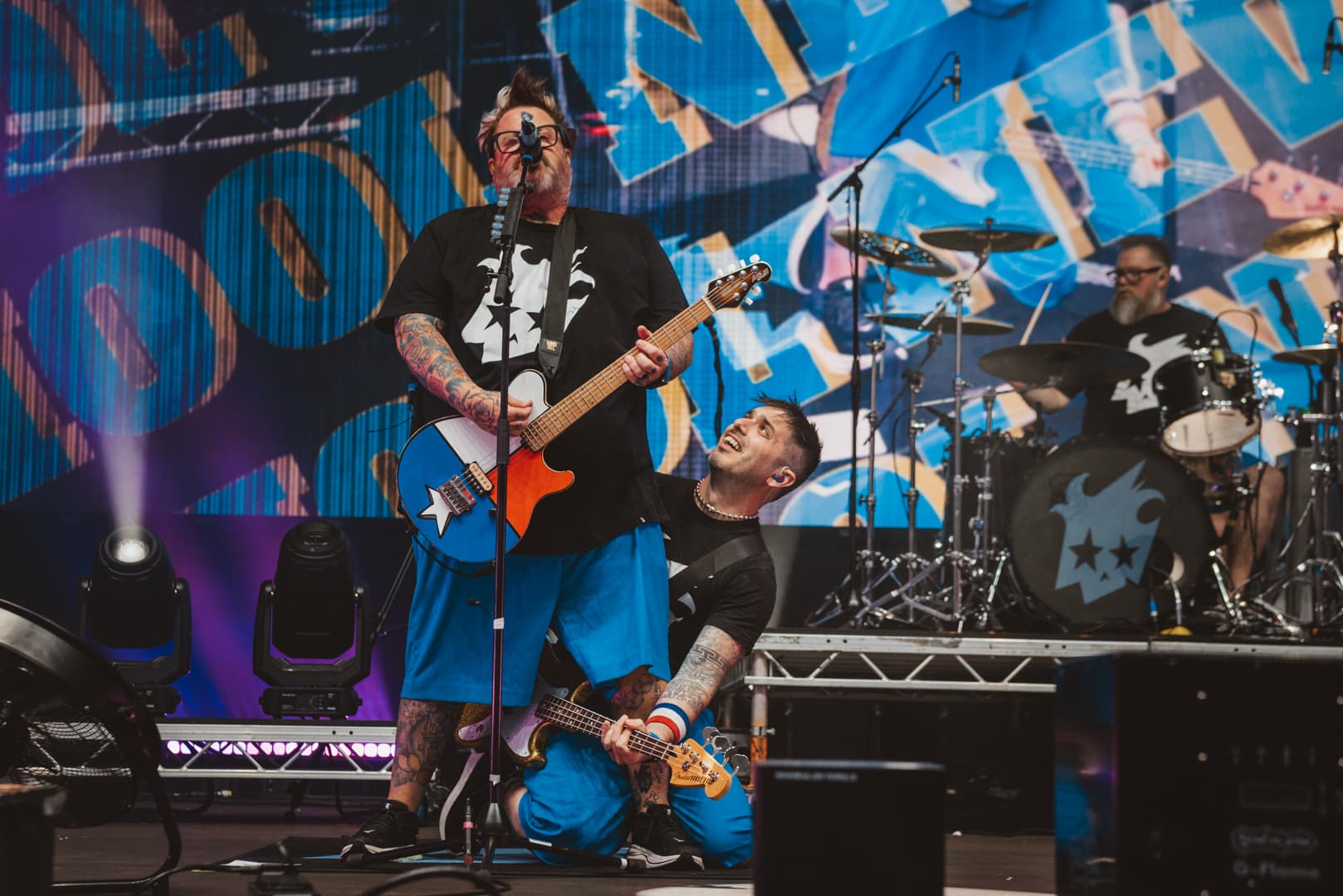 Band performing energetically on stage with colorful backdrop