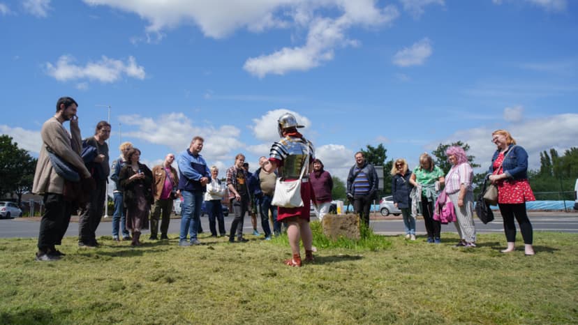 Guide in Roman armor speaking to tourists on grassy area
