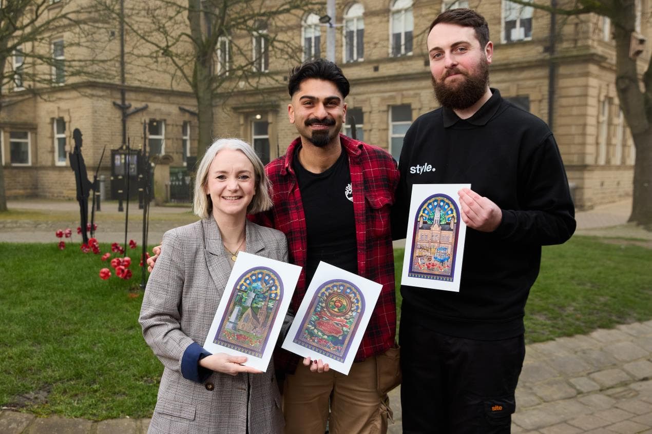 Three people hold colorful mural designs in front of a historic building in Ossett, surrounded by greenery and flowers.