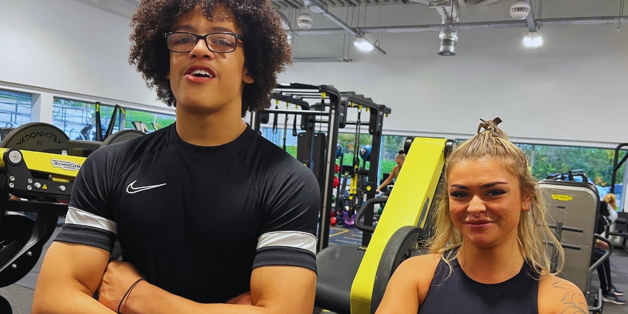Two people smiling in a modern gym with fitness equipment