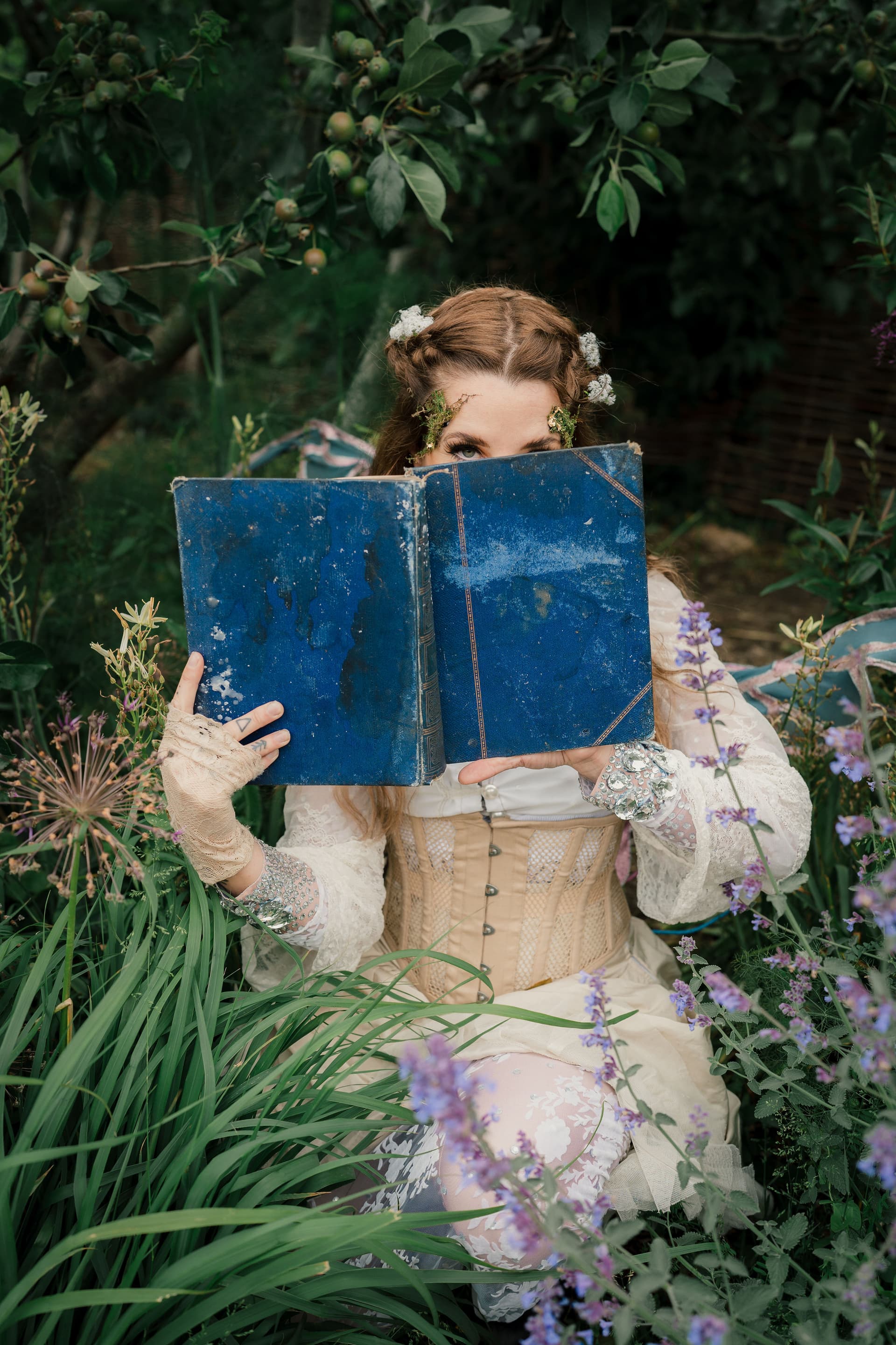 Woman in vintage dress reading a blue book in a garden