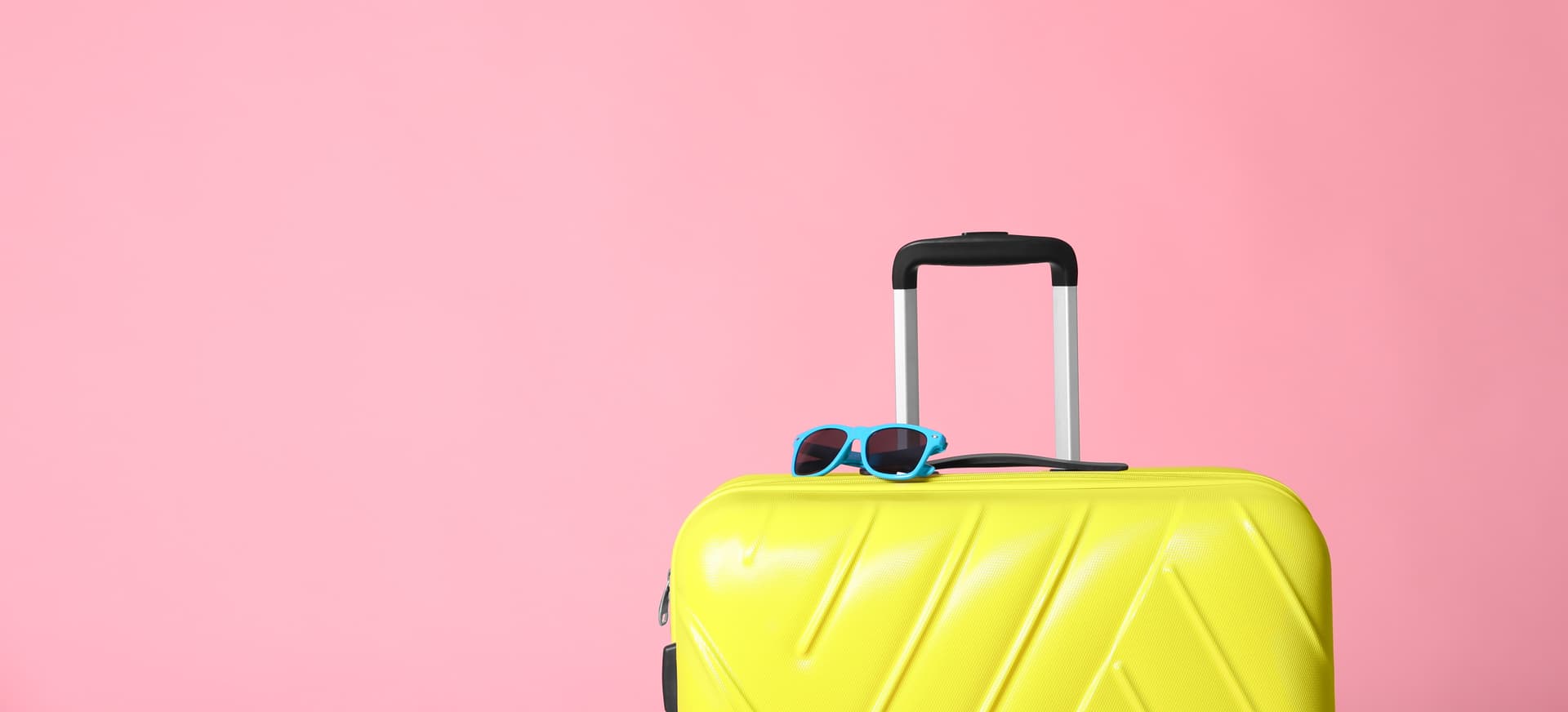 Bright yellow suitcase with blue sunglasses on pink background