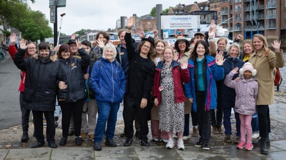 Group of tourists waving by riverside in York with city buildings