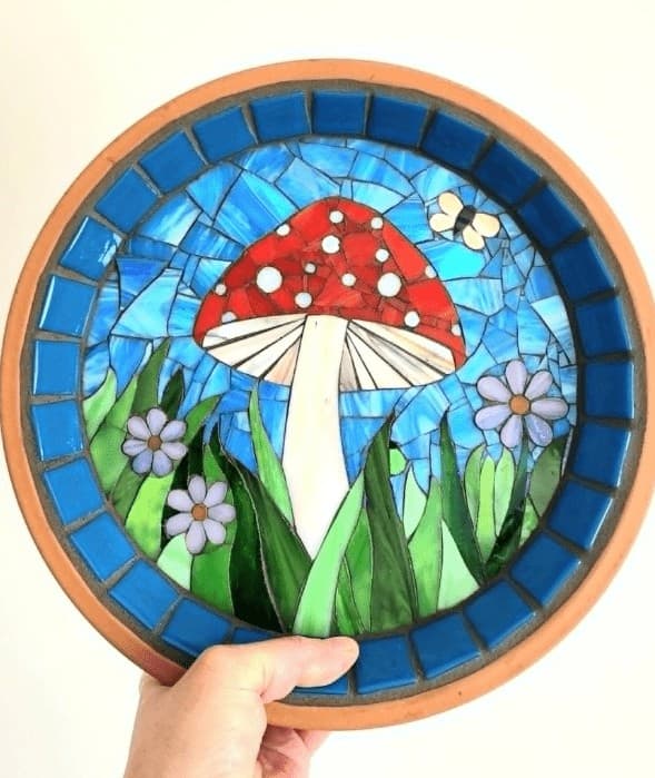 Hand holding a mosaic plate with red mushroom and flowers