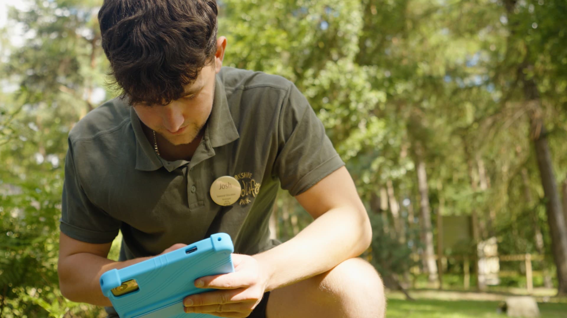 Young man in green polo using tablet in forested area