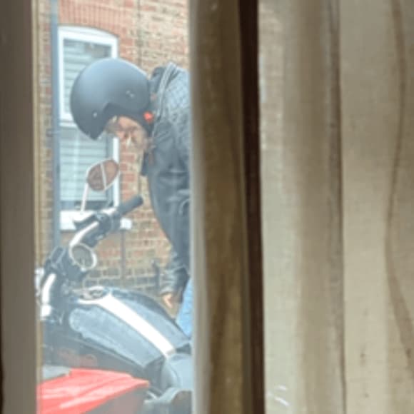 Person in black helmet beside motorcycle near brick wall