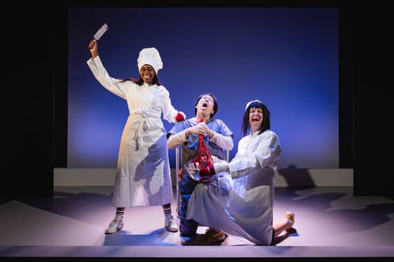 Three actors in dramatic culinary-themed costumes on stage