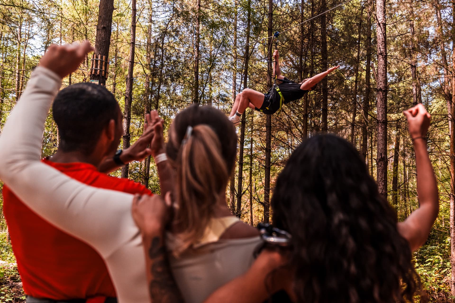 Group cheering as person zip-lines through forest