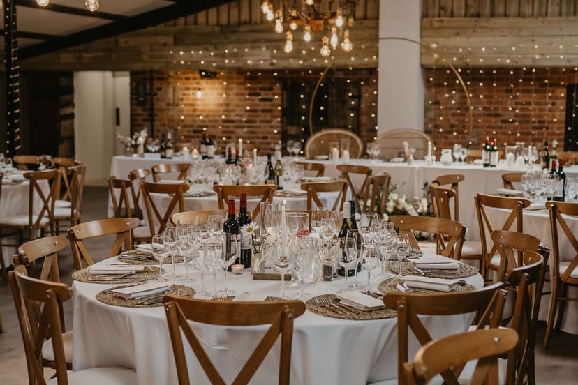 Elegant round tables set with fine glassware and rustic wooden chairs, adorned with soft lighting and floral centerpieces at Deighton Lodge.