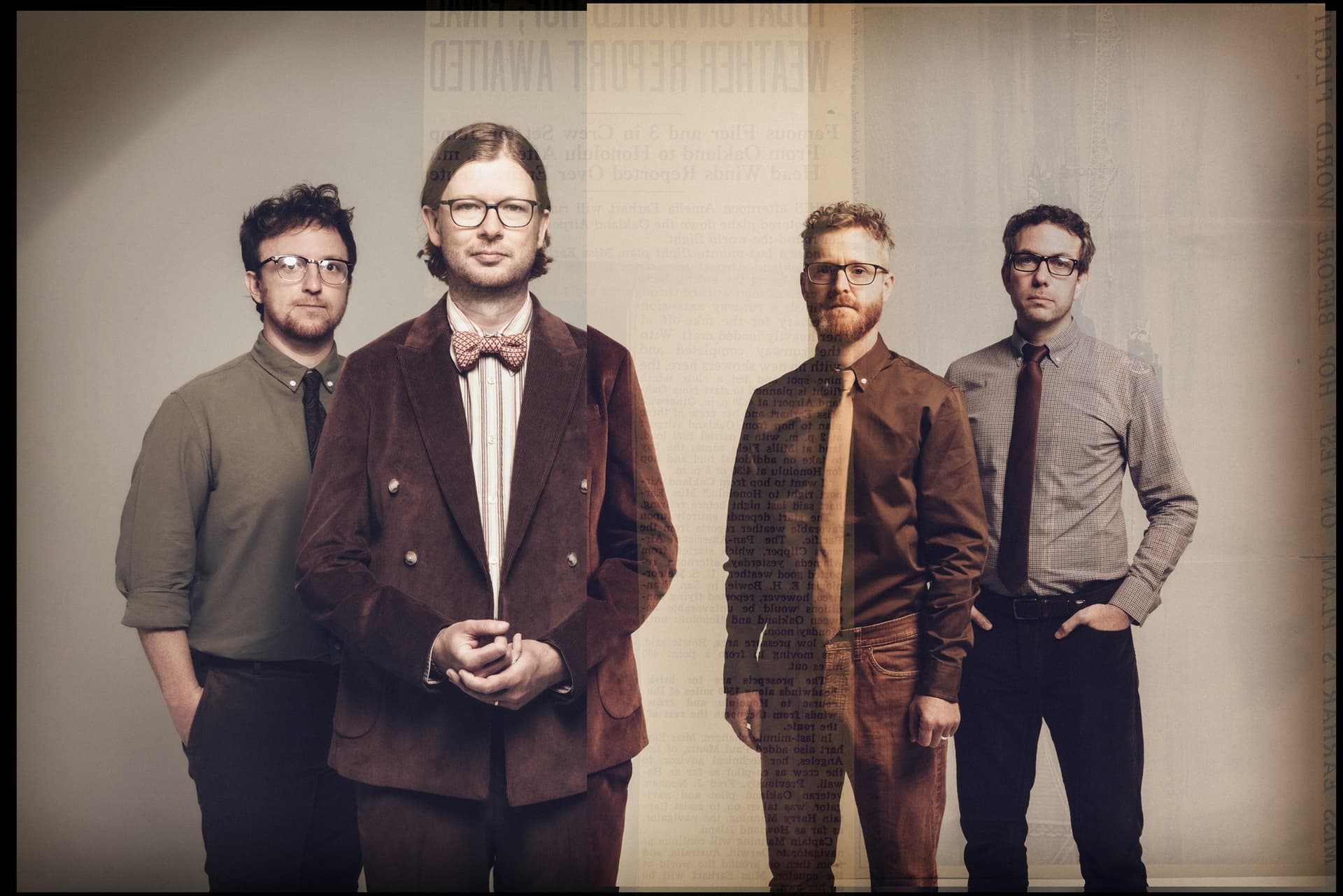 Four musicians pose together, dressed in stylish attire, with a vintage backdrop hinting at a historical atmosphere.
