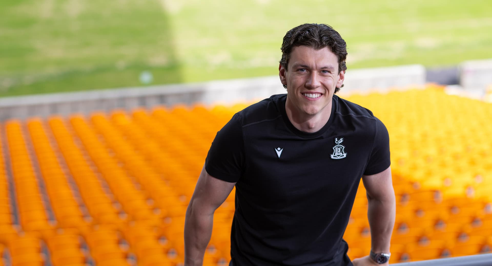 Smiling man in black shirt standing in a stadium with orange seats