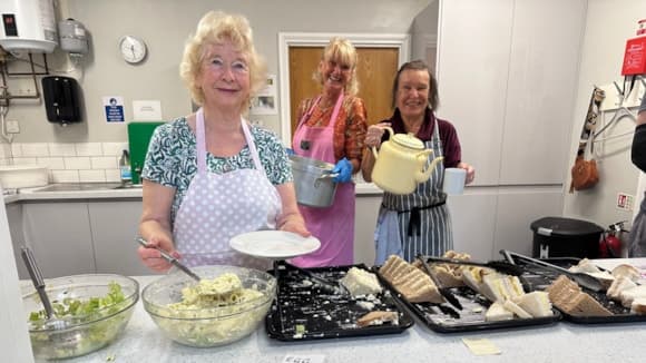 Three women in aprons serving food in a community kitchen