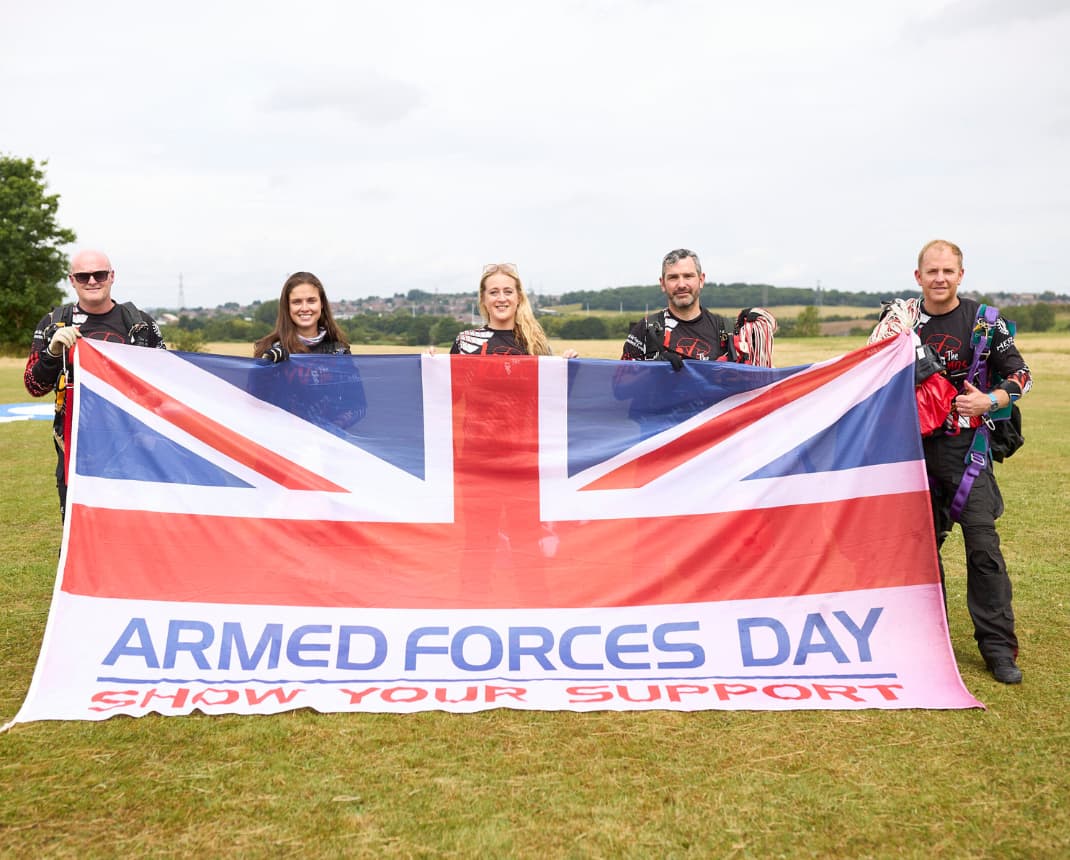 Group holding Armed Forces Day flag on grassy field