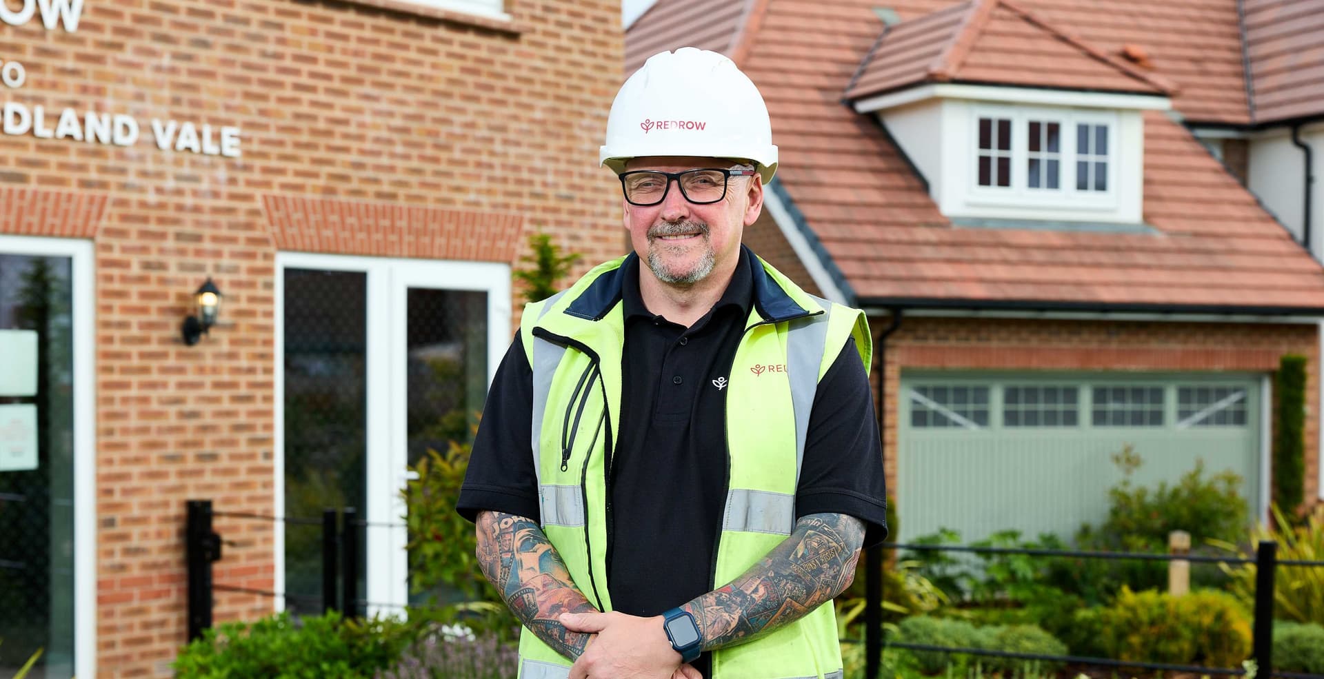 Smiling construction worker in high-vis vest in front of brick houses
