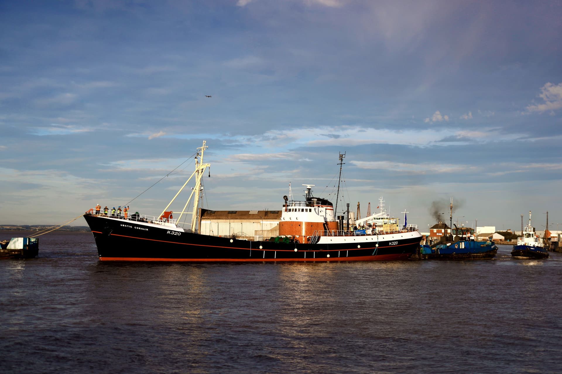Fishing trawler on calm waters with industrial docks in background