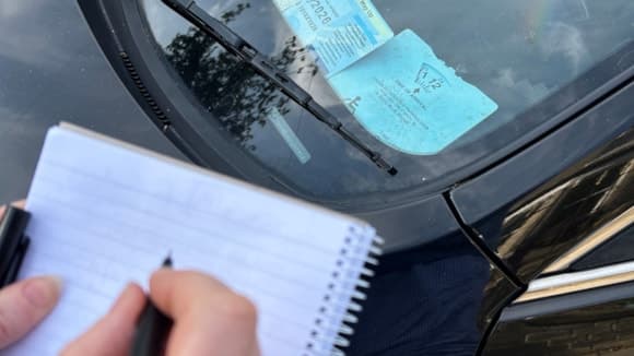 Close-up of a person writing on a notepad beside a car windshield
