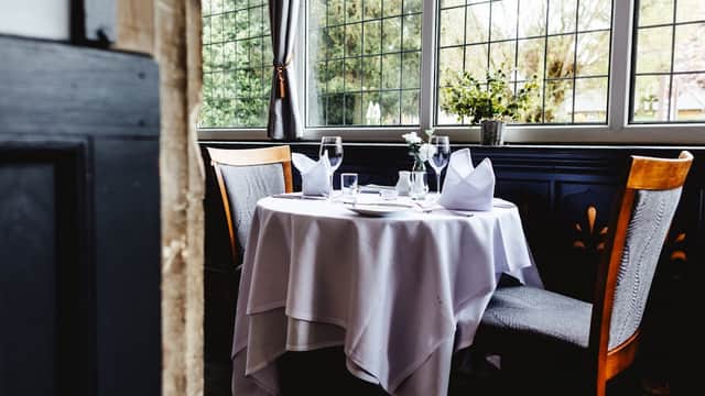 Elegant dining table set with white tablecloth, glassware, and napkins, surrounded by large windows and greenery.