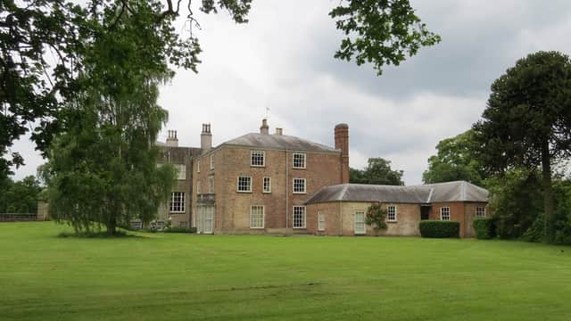 Historic brick estate surrounded by lush green lawn and trees under a cloudy sky in Scampston, Yorkshire.
