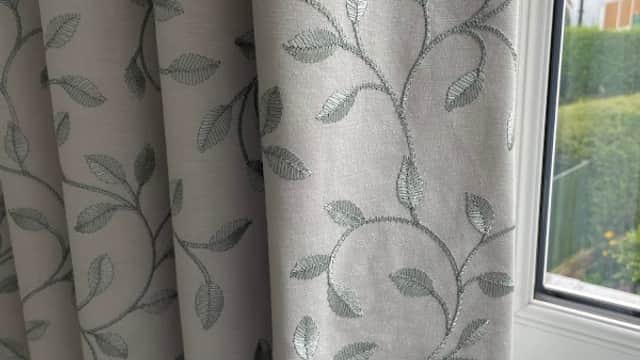 Light-colored curtains with a delicate leaf pattern, hanging by a window with greenery visible outside.
