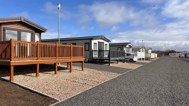 Modern caravans with wooden decks lined along a gravel path under a partly cloudy sky at Coatham Caravan Park.