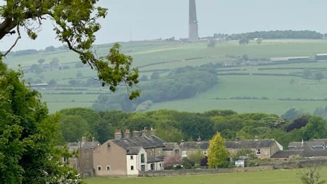 Lush green fields with a distant tower, surrounded by quaint houses and trees under a cloudy sky.