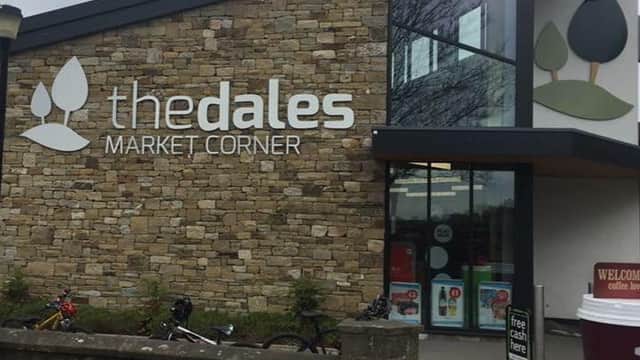 Modern stone building with large windows, featuring "the dales MARKET CORNER" signage and bicycles parked outside.