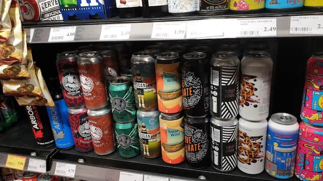 Cans of various beverages on a grocery shelf, with colorful labels and prices displayed underneath.