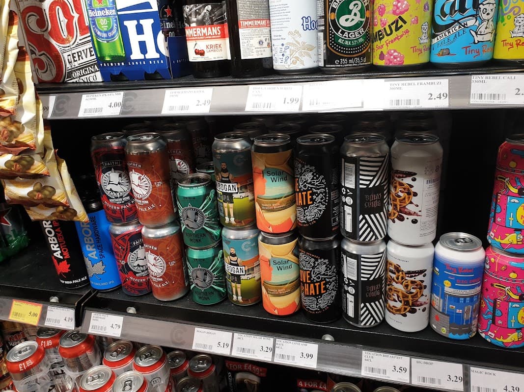 Cans of various beverages on a grocery shelf, with colorful labels and prices displayed underneath.