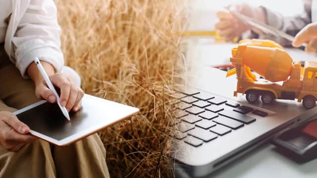 A person writes on a tablet beside a toy cement mixer and a laptop with a level tool on a desk.
