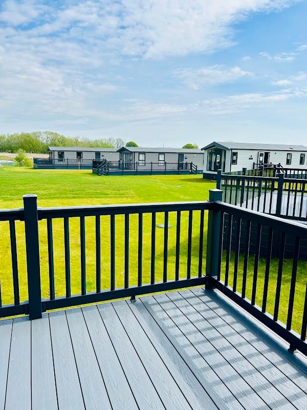 View from a deck overlooking green grass, holiday homes, and a serene lake under a blue sky with scattered clouds.