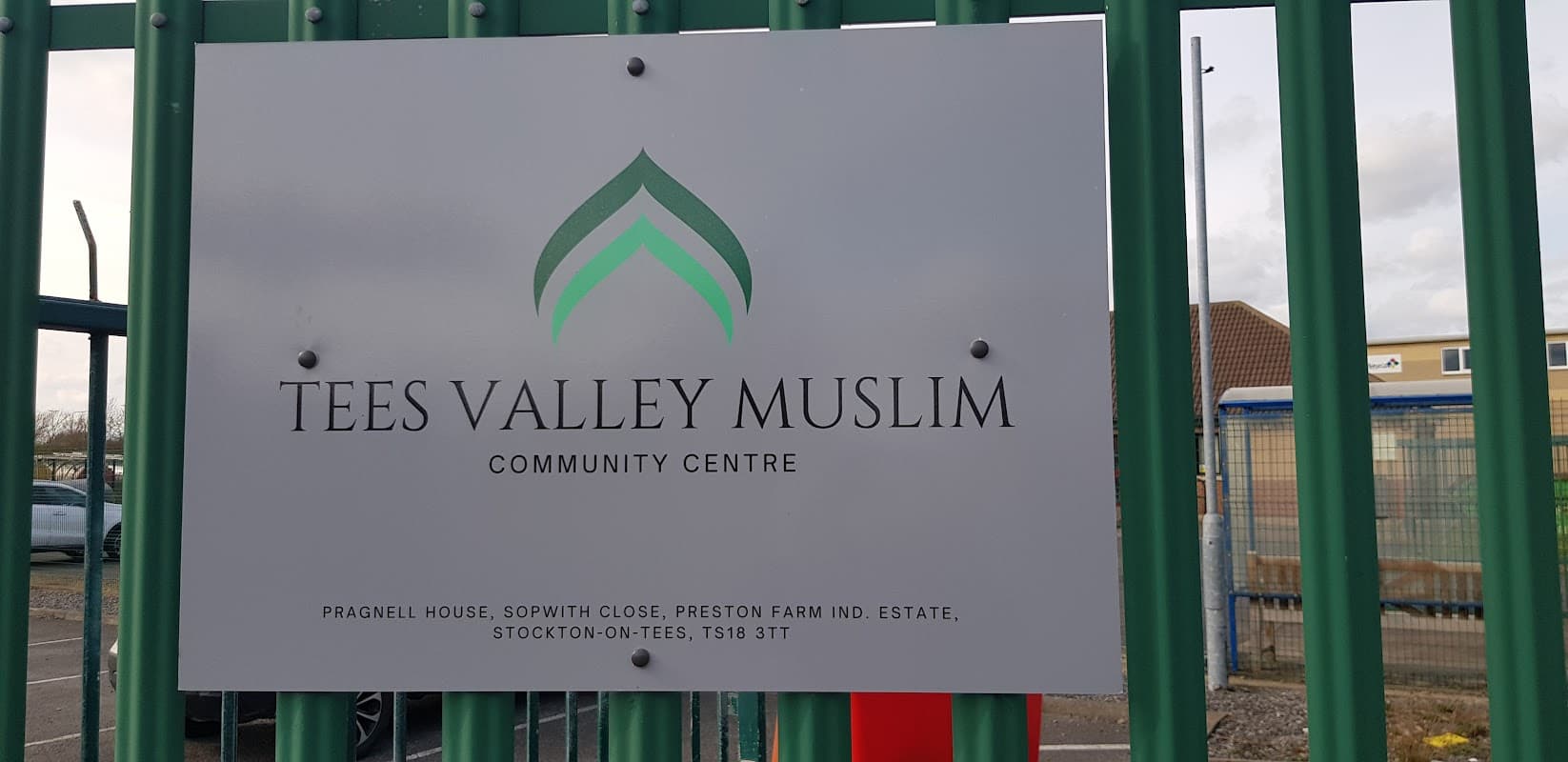 Sign for Tees Valley Muslim Community Centre, featuring green and white logo on a metal fence.