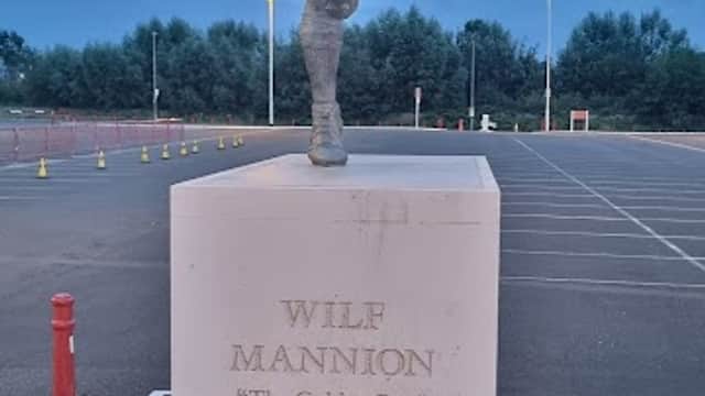 Statue of Wilf Mannion, a footballer, with a cloudy sky and empty car park in the background.